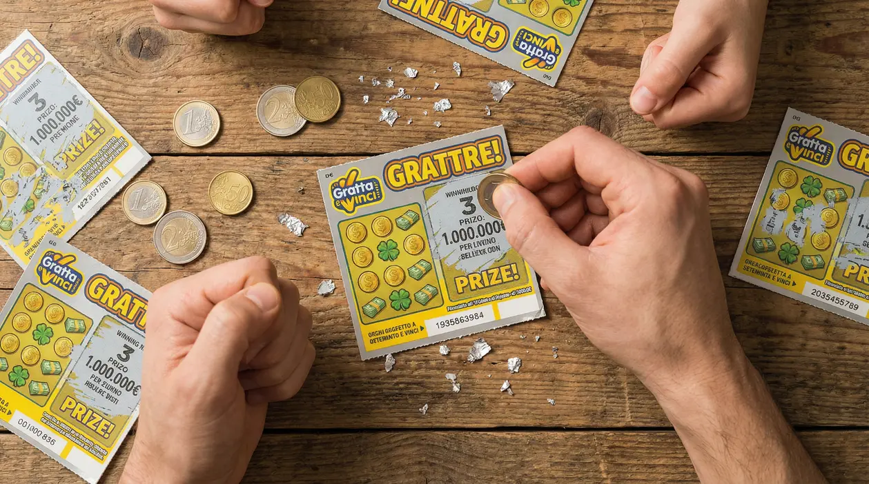 Mani che grattano un biglietto Gratta e Vinci su un tavolo di legno, con monete e pezzi di pellicola argentata