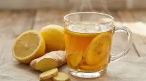 Tisana calda allo zenzero e limone in tazza di vetro, con fette di limone e radice di zenzero su tavolo