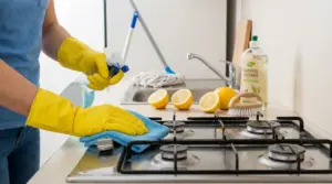 Persona con guanti gialli pulisce il piano cottura con panno e spray in una cucina