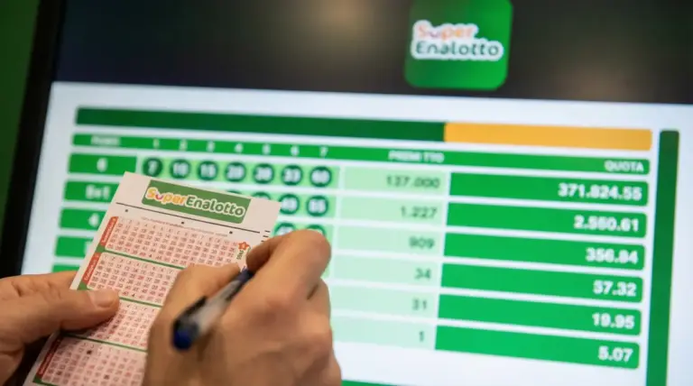 Mani che compilano una schedina del SuperEnalotto davanti a uno schermo con i risultati e le quote della vincita